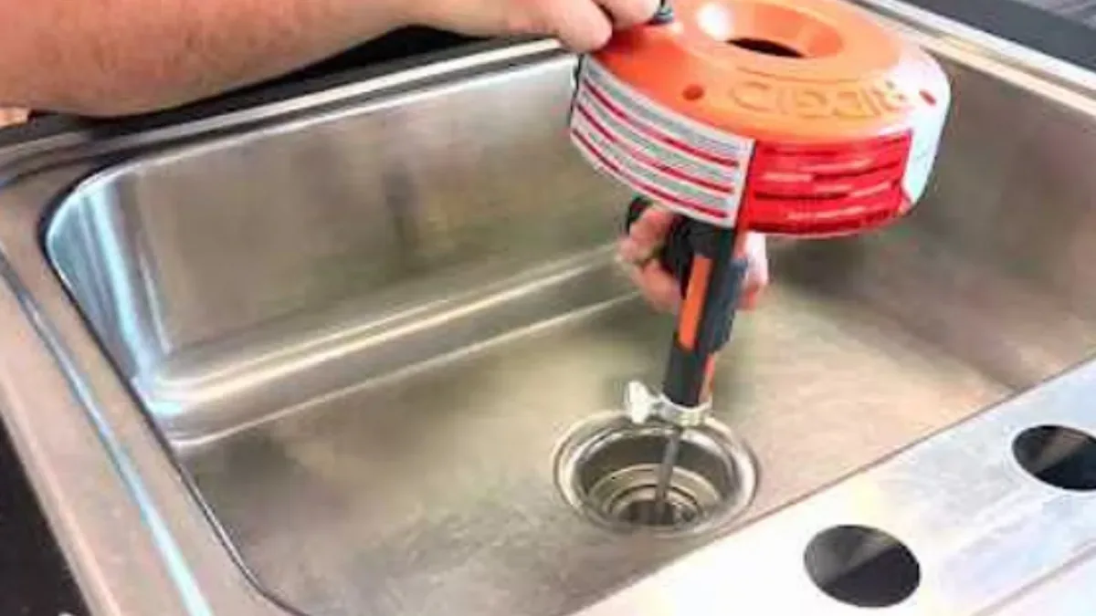 Hand-crank drain auger being fed into a sink drain to clear a slow draining sink
